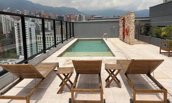 A rooftop pool with a city view, wooden loungers, and a stone wall with a red pipe. - Spectacular apartment in the town, surrounded by nature, parks and restaurants. (Medellín)
