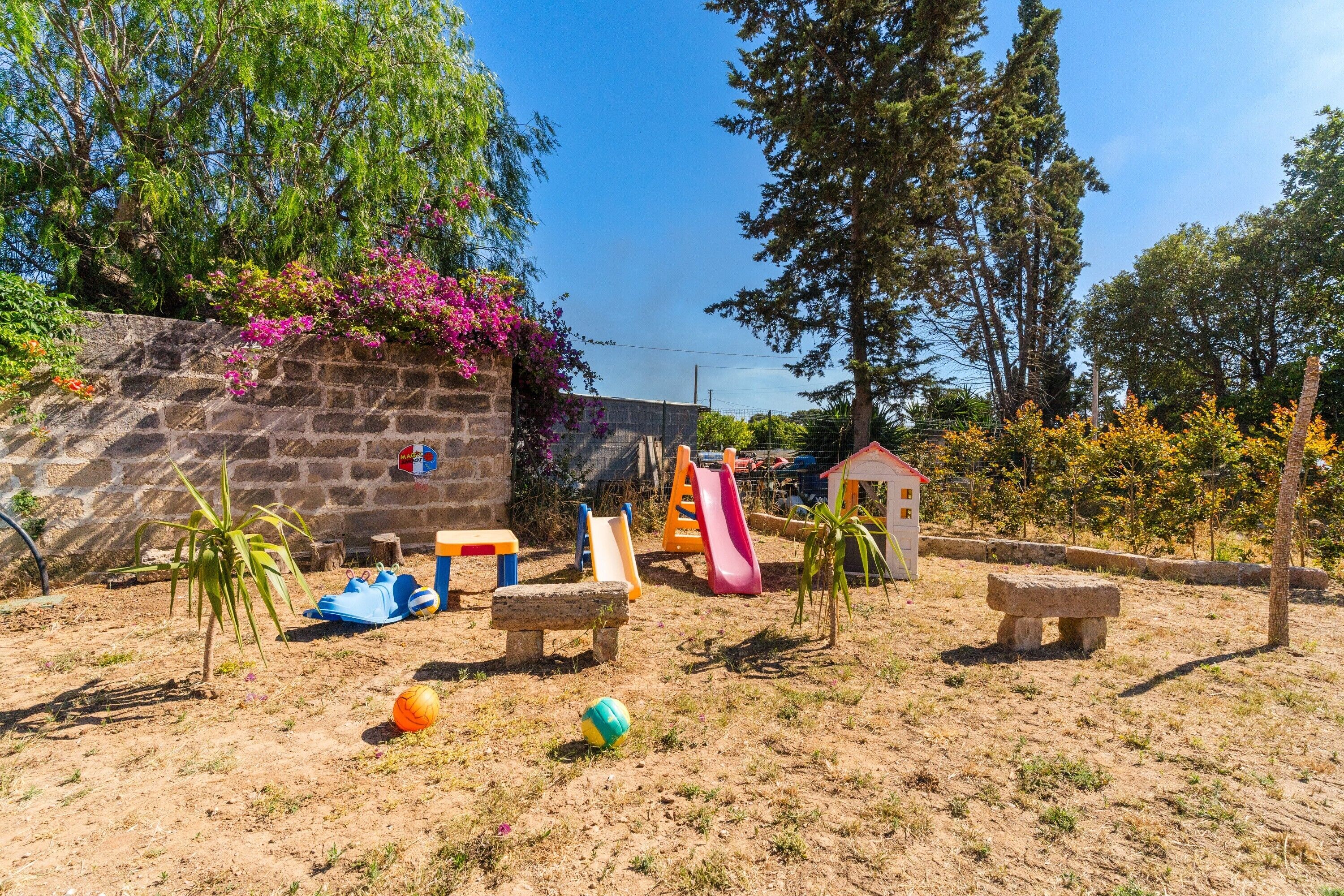 Un'area giochi con scivoli e panchine, circondata da alberi e un muro in pietra.