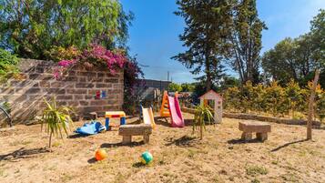 Un'area giochi con scivoli e panchine, circondata da alberi e un muro in pietra.