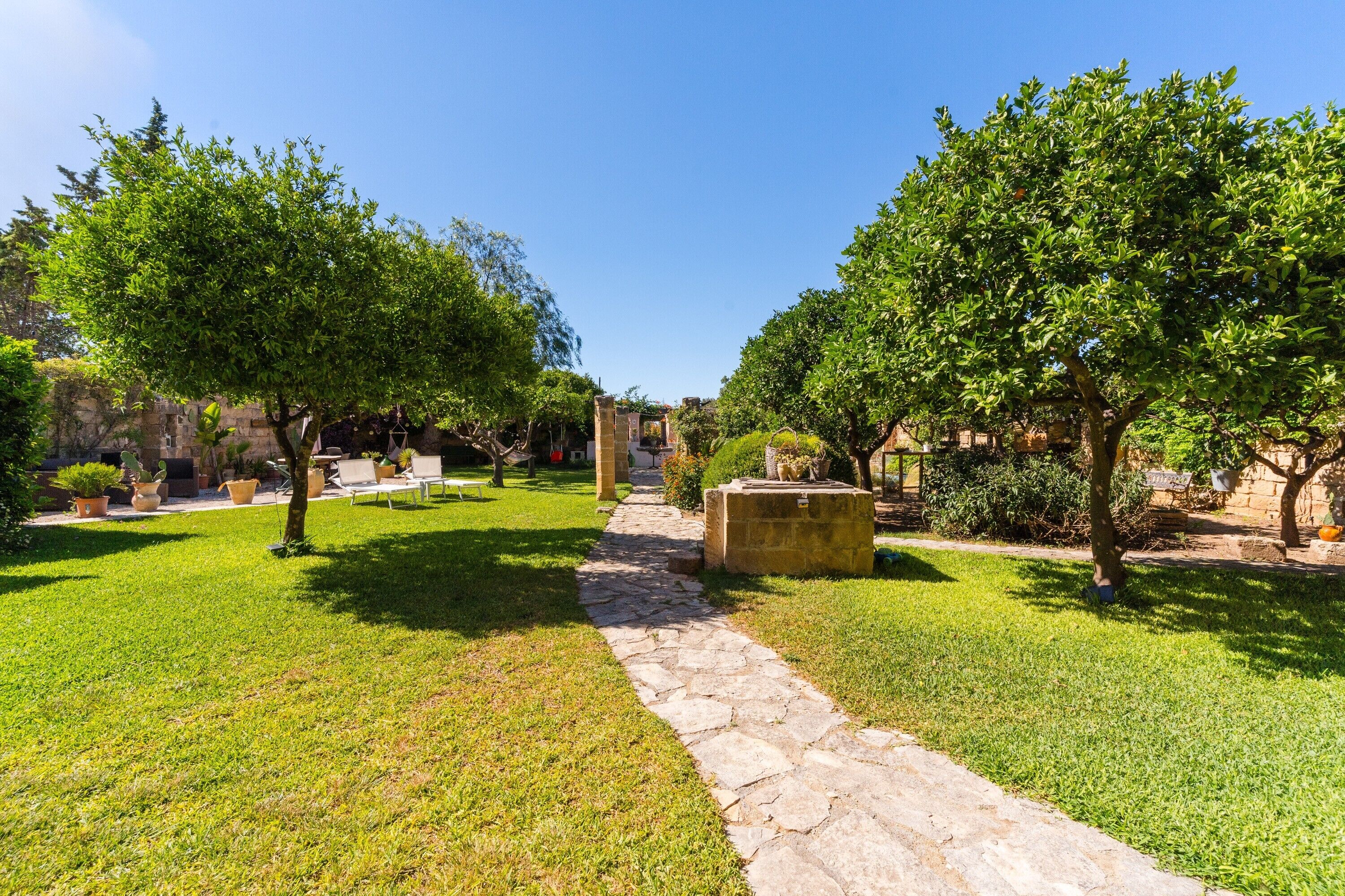 Um caminho de pedra serpenteia por um jardim bem cuidado, com árvores e plantas em vasos.