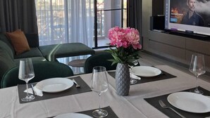 Habitación de hotel con comedor, sofá, televisor y balcón con cortinas.