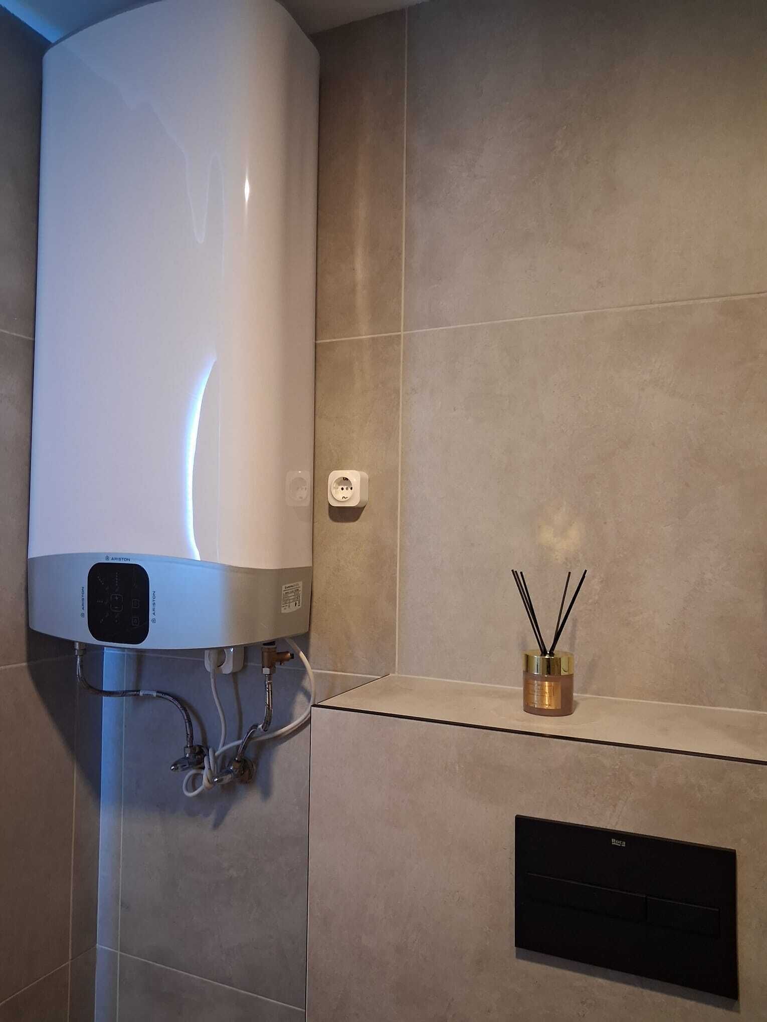 Un bagno con uno scaldabagno bianco, una presa a muro e un piccolo ripiano con un diffusore di stoppino.