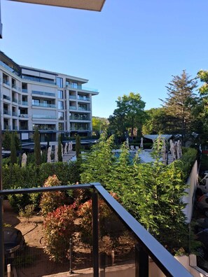 Ein modernes, mehrgeschossiges Gebäude mit Balkonen, einem Poolbereich und umliegender Bepflanzung.
