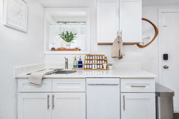 A white kitchen with a window, a sink, a wooden spice rack, and cabinets.