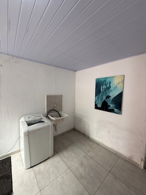 A small, clean bathroom with a washing machine, a sink, and a poster on the wall.