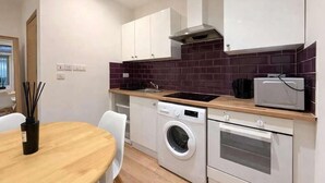 Cocina compacta con lavadora, horno, microondas y comedor con mesa y sillas.