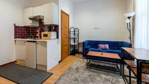 Un espacio habitable compacto con kitchenette, un sofá, una mesa pequeña y una lámpara.