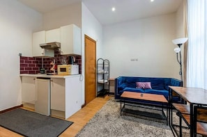 Un espacio habitable compacto con kitchenette, un sofá, una mesa pequeña y una lámpara.