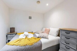 A bedroom with a bed, a bedside table, a dresser, and a wall-mounted light fixture. - Earls Court Apt, Sleeps 3 With Private Entrance (London)