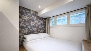Un dormitorio con cama, ventana y pared con estampado floral.