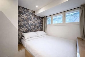 Un dormitorio con cama, ventana y pared con estampado floral.