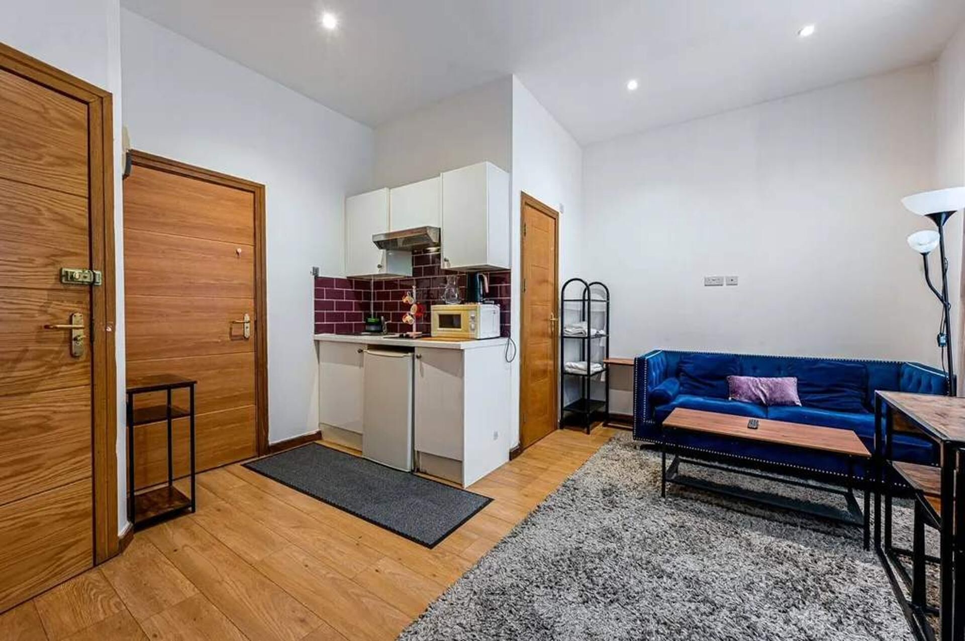 Ein kompakter Wohnraum mit Küchenzeile, einem blauen Sofa, einem kleinen Tisch und einer Lampe.