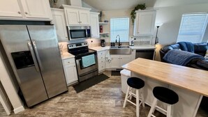 A compact kitchen with a refrigerator, stove, microwave, and sink. There are two stools at a wooden table.