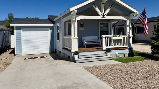 A single-story house with a garage, a porch with a bench, and an American flag.