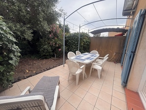 A patio with a table and chairs, surrounded by greenery and a covered area. - Bright house with terrace and garden in Fréjus (Fréjus)