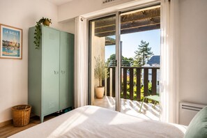 Ein Schlafzimmer mit einem Bett, einem grünen Kleiderschrank, einer Topfpflanze, einem Korbwannenmöbel und einem Balkon mit Aussicht.