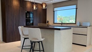 Uma cozinha moderna com uma ilha central, banquetas, iluminação pendente e uma grande janela com vista.
