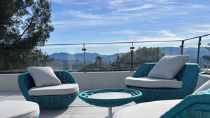 Um terraço com móveis de vime, uma mesa redonda e vista para as montanhas.