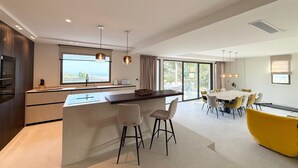 Uma cozinha moderna com uma ilha central, uma área de refeições com uma cadeira amarela e uma grande janela com vista.