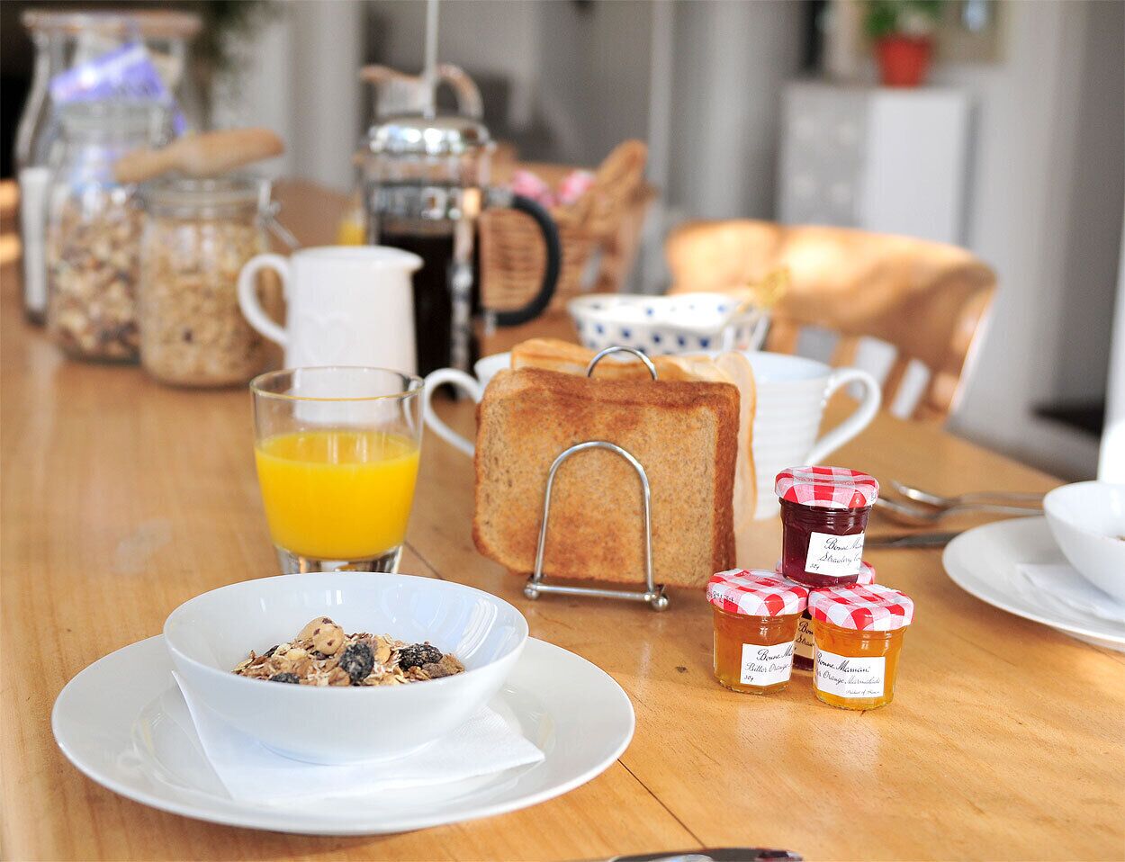 A breakfast table with toast, cereal, juice, and honey jars.