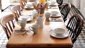 Un comedor con una larga mesa de madera dispuesta para una comida, rodeada de sillas, con una lámpara colgante arriba.