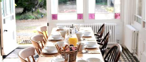 A dining area with a long wooden table set for a meal, surrounded by chairs, with a hanging light fixture above.
