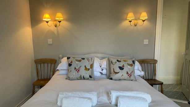 Una cama bien hecha con ropa blanca, dos lámparas de pared y dos sillas.