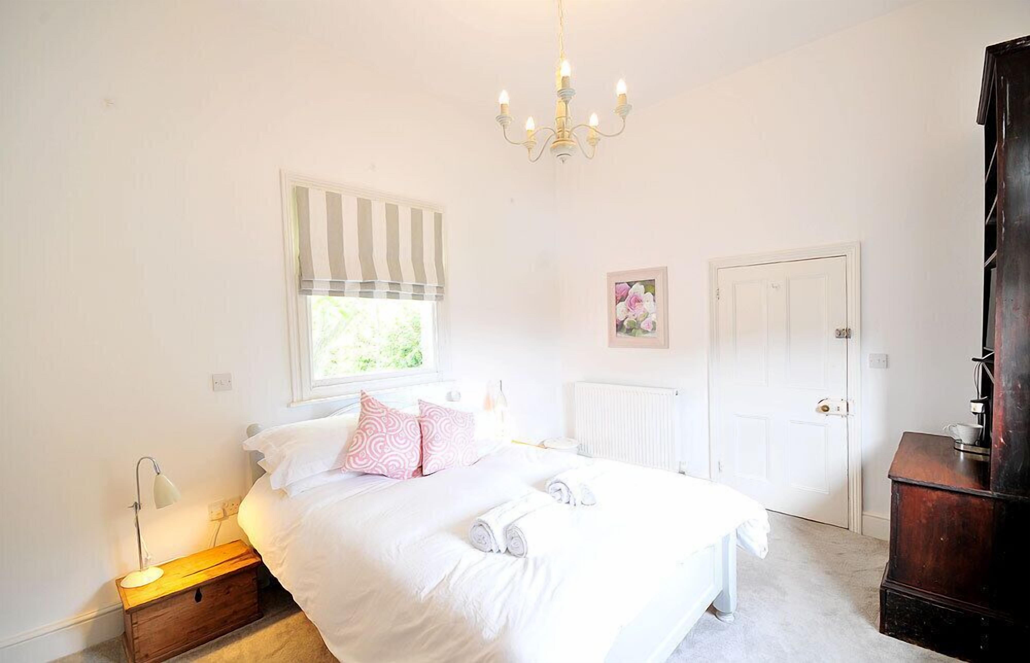 A bedroom with a bed, bedside lamp, window with blinds, radiator, and a door.