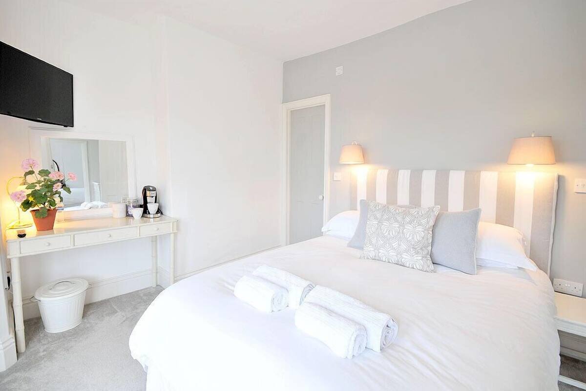 A hotel room with a bed, bedside lamps, a desk with a mirror, a trash bin, and a potted plant.