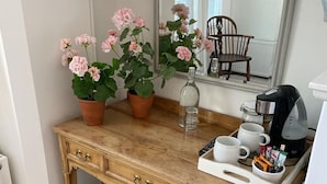 Un escritorio de madera con un espejo, dos plantas en macetas, una cafetera y una bandeja con tazas y un control remoto.