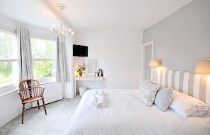 A bedroom with a large bed, a desk, a chair, a television, and a window with curtains.