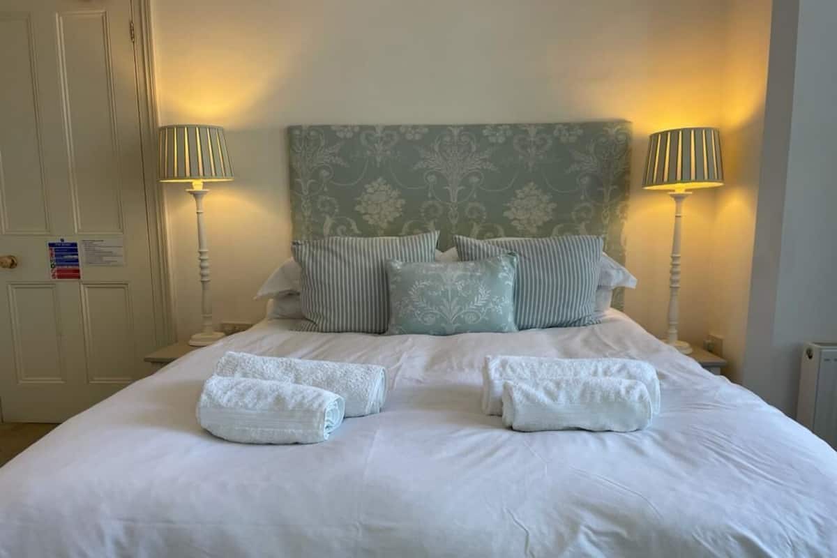A neatly made bed with white linens and pillows, two bedside lamps, and a patterned headboard.
