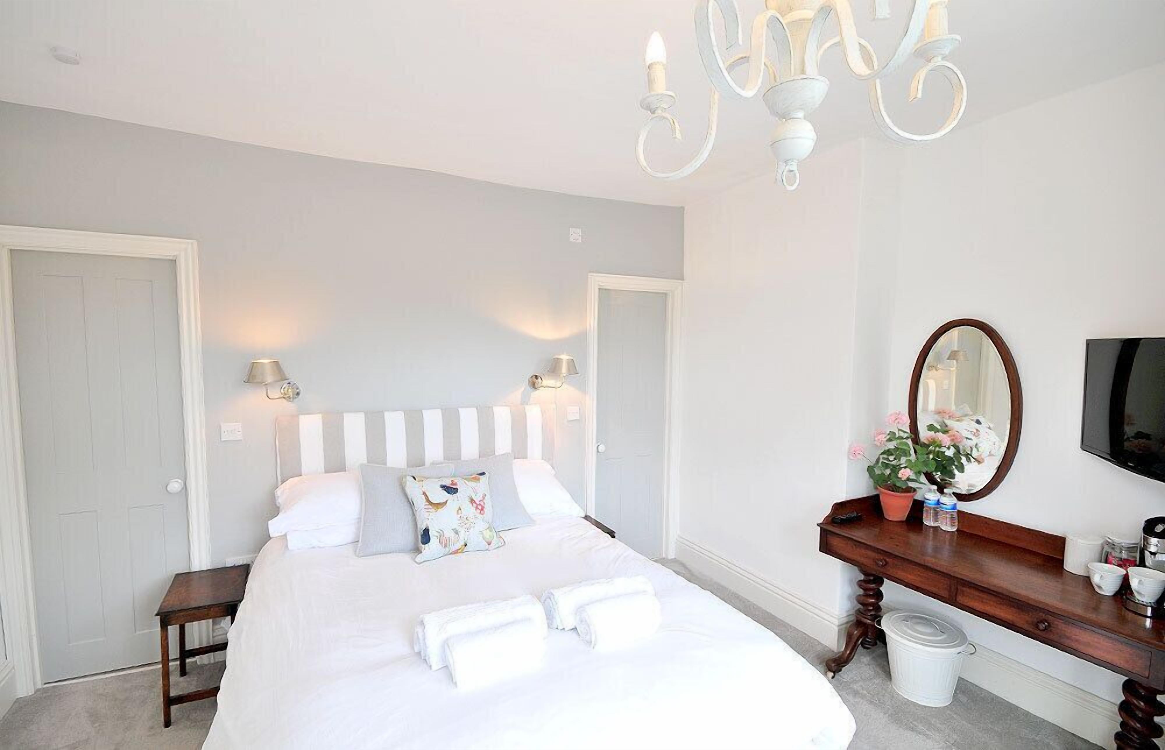 A bedroom with a bed, bedside lamps, a dresser, a mirror, and a TV.
