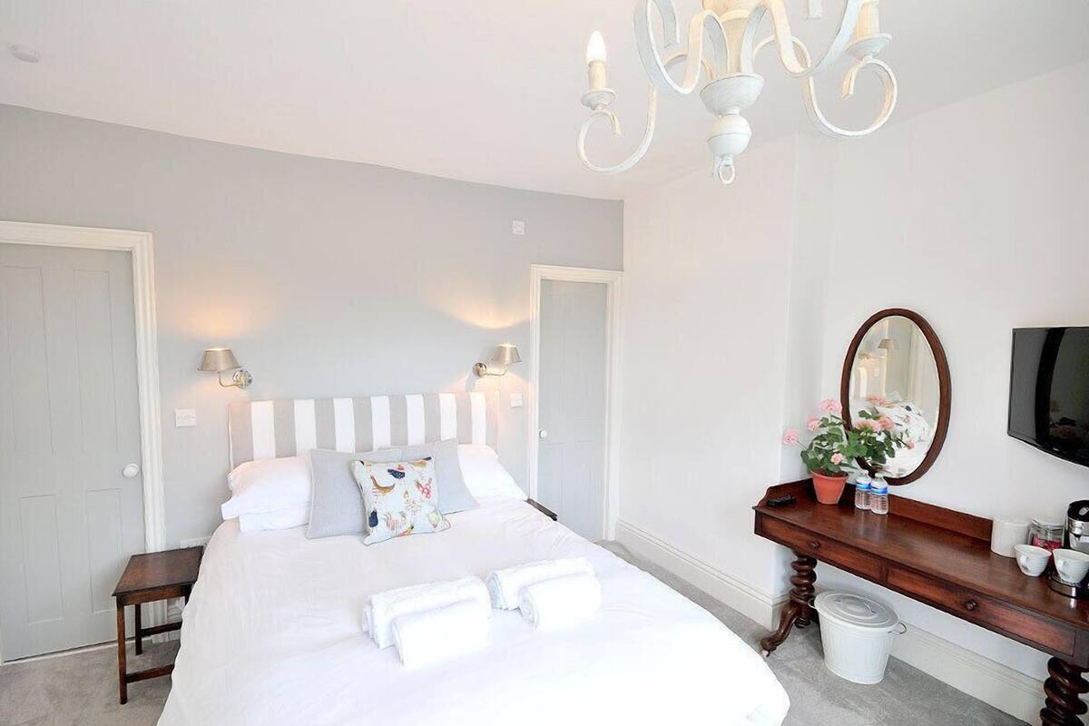 A bedroom with a bed, bedside lamps, a dresser, a mirror, and a TV.