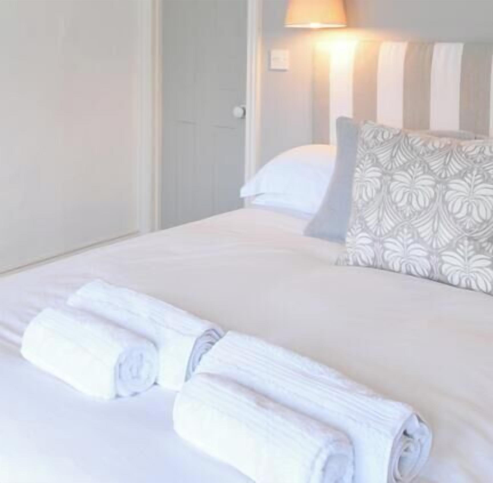 A neatly made bed with pillows, a bedside lamp, and rolled towels.