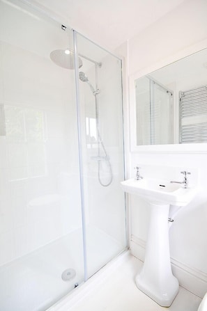 A modern bathroom with a glass-enclosed shower, a white pedestal sink, and a large mirror.