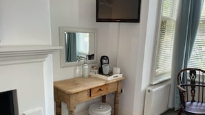 Una habitación con escritorio de madera, un espejo, un televisor, un radiador, una silla y una ventana con persianas.