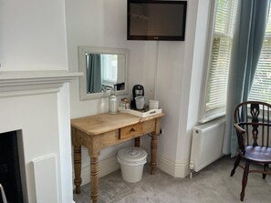 A room with a wooden desk, a mirror, a television, a radiator, a chair, and a window with blinds. - Poplars Farm (Henlow)