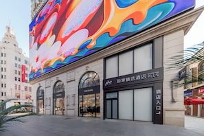 A hotel with a modern facade, a large digital billboard, and storefronts including 'YOUNGOR' and 'HOMELINN PLUS'.