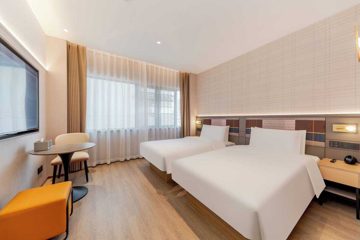 A hotel room with two beds, a small table, a chair, a desk, and a TV.
