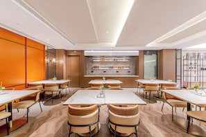 Un comedor moderno con varias mesas y sillas, una zona de bar central con estanterías y vistas a la cocina.
