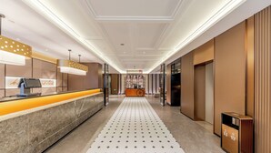 Zona de recepción de hotel con mostrador de mármol, quiosco digital y mostrador de recepción.
