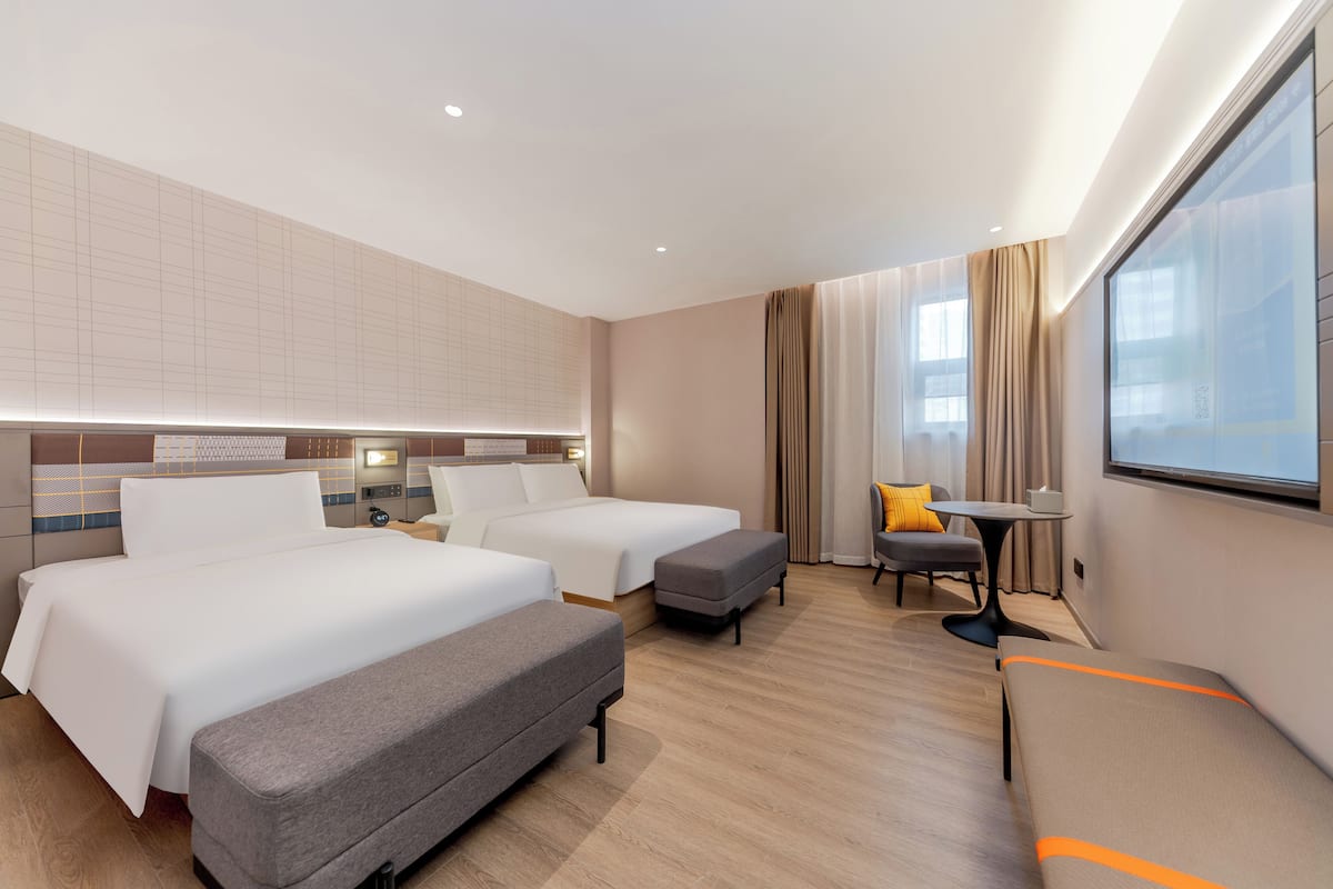 A hotel room with two beds, a sofa, a small table, and a window.