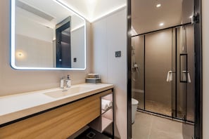 A modern bathroom with a large mirror, a sink, a vanity, and a glass shower enclosure.