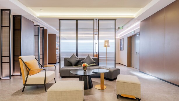 Un vestíbulo moderno con un sofá, sillones, una mesa de centro y vistas a través de un panel de vidrio.
