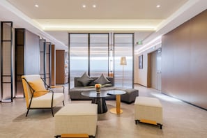 Un vestíbulo moderno con un sofá, sillones, una mesa de centro y vistas a través de un panel de vidrio.