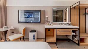 Habitación de hotel con cama, escritorio, silla, televisor montado en la pared, espejo y armario.