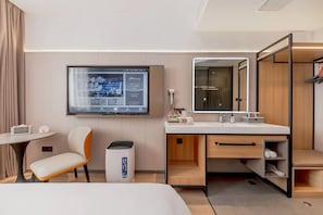 Habitación de hotel con cama, escritorio, silla, televisor montado en la pared, espejo y armario.