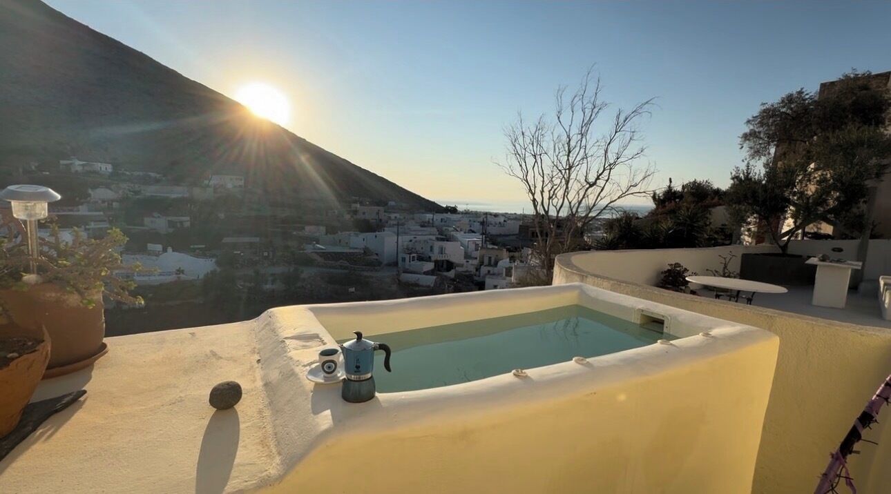 A rooftop terrace with a pool, a coffee maker, and a view of a town and mountain.