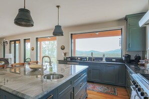 Una cocina moderna con una isla grande, armarios oscuros y vistas a las montañas a través de un amplio ventanal.